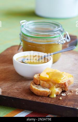 Honigsenf auf Brot mit Käse auf Holzbrett mit Becher und Löffel im Hintergrund Stockfoto