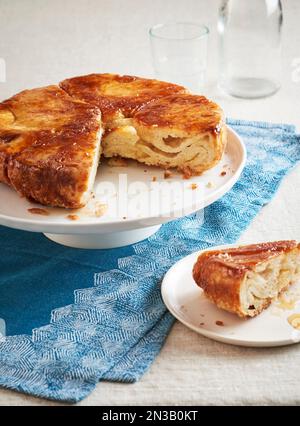 Kouign Amann auf einem Kuchenstand, mit einem Stück, das man herausnimmt und auf einem Dessertteller vor dem Hotel serviert Stockfoto