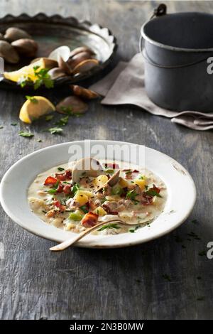 Schüssel mit Muschelsuppe auf einem grauen Holztisch mit Zutaten im Hintergrund Stockfoto