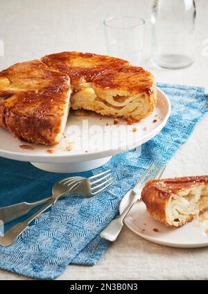 Kouign Amann auf einem Kuchenstand mit einem Stück, das herausgenommen und auf einem Dessertteller mit Gabeln davor serviert wird Stockfoto