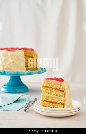 Vanille-Rhabarber-Kuchen auf einem türkisfarbenen Kuchenstand mit einem Stück herausgenommen und serviert auf einem Dessertteller mit Gabel auf weißem Hintergrund Stockfoto