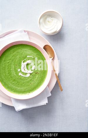 Aspsargussuppe mit goldfarbenem Löffel und einer Beilage Creme Fraiche auf blau gestreiftem Hintergrund Stockfoto