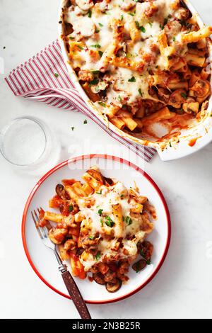 Gebackene Ziti mit Pilzen in einem Auflauf mit einer Portion auf einem Teller mit einer Gabel davor Stockfoto