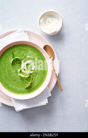 Aspsargussuppe mit goldfarbenem Löffel und einer Beilage Creme Fraiche auf blau gestreiftem Hintergrund Stockfoto