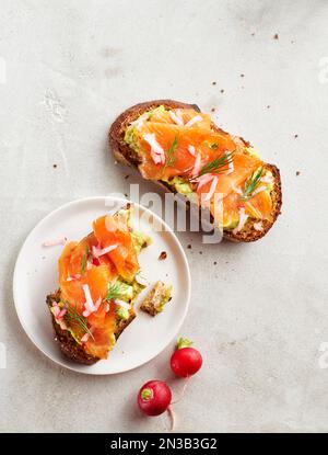 Avocado-Toast mit geräuchertem Lachs, Dill und Rettich auf grauem Hintergrund Stockfoto