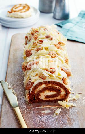Weiße Schokoladenkuchenrolle auf einem Schneidebrett mit Messer Stockfoto