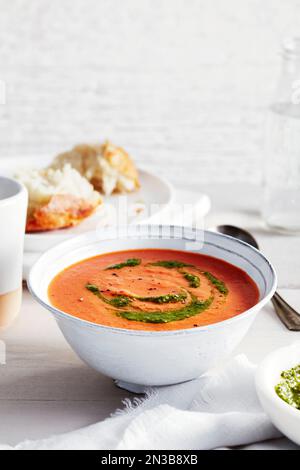 Tomatensuppe mit Pesto und eine Seite knuspriges Brot im Hintergrund Stockfoto