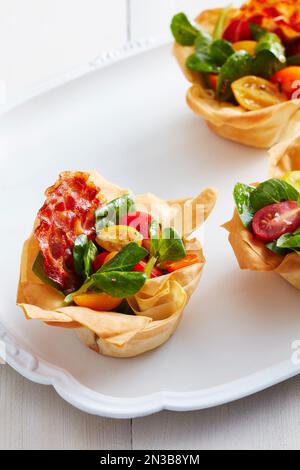 Phyllo-Becher mit Speck und Tomaten auf einer weißen Platte Stockfoto