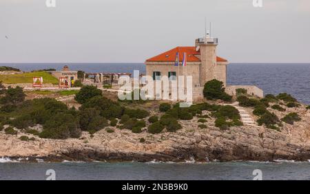 OTOCIC-GASTGEBER, VIS, KROATIEN, EUROPA - Leuchtturm auf der Host-Insel in der Nähe des Hafens von Vis, wie von Fort George aus gesehen, und Leuchtturm-Gebäude. Stockfoto