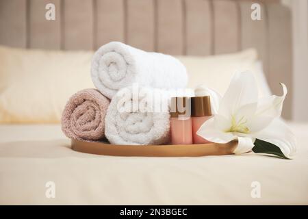 Gerollte saubere Handtücher, Blumen- und Shampooflaschen auf dem Bett Stockfoto