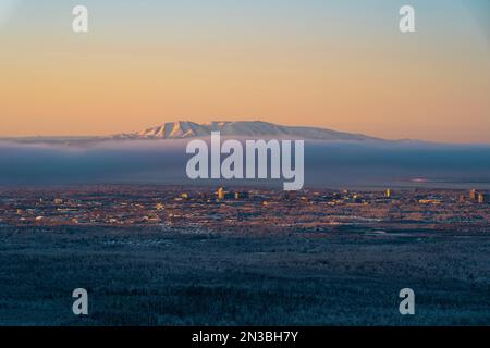 Die Sonne untergeht auf dem Mt. Susitna oder Sleeping Lady, gegenüber Cook Inlet von Downtown Anchorage, Alaska auf Dena’ina Land, mit Nebel und Knik Arm im Blick Stockfoto