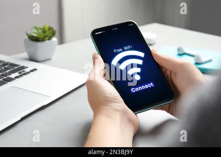 Frau, die sich mit einem Mobiltelefon am Tisch mit WLAN verbindet, Nahaufnahme Stockfoto