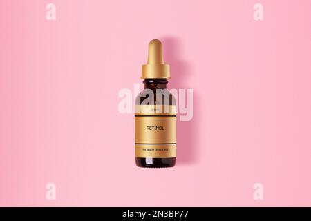 Retinol in einem glasbraunen Kosmetikgefäß. Mit goldenem Etikett. Mit einer Inschrift. Auf pinkfarbenem Hintergrund. Stockfoto