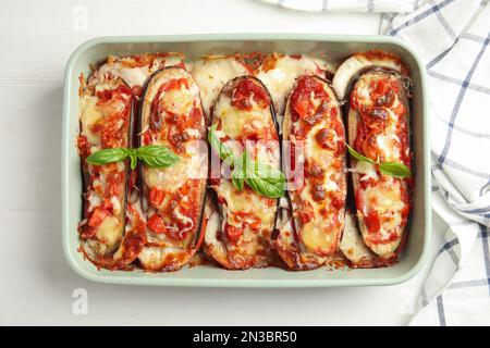 Gebackene Aubergine mit Tomaten, Käse und Basilikum in Geschirr auf weißem Holztisch, flach liegend Stockfoto