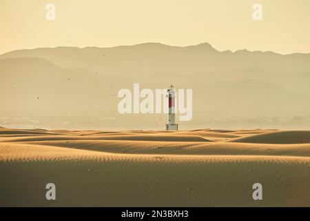 Leuchtturm mit roten Streifen auf den gewellten Sanddünen im Abendlicht bei Sonnenuntergang, Ebro River Delta; Katalonien, Spanien Stockfoto