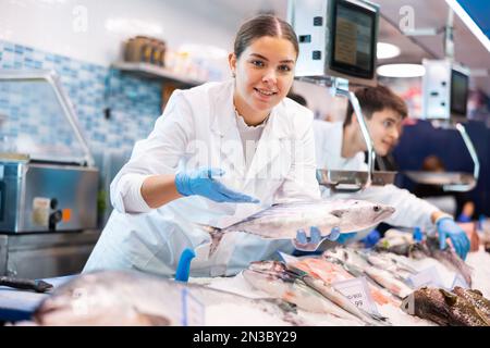 Positive Verkäuferin, die Bonitofisch im Fischladen vorführt Stockfoto