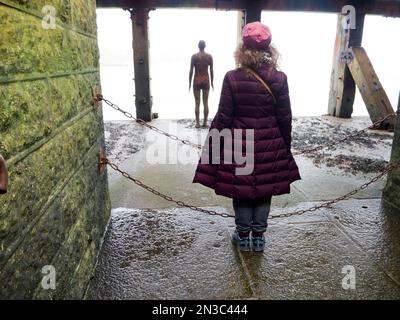 Blick von hinten auf eine Frau, die sich als Antony Gormleys gusseiserne Figur ausgibt, ein anderes Mal 1999-2013, mit Blick auf das Meer vom Folkestone H.. Stockfoto