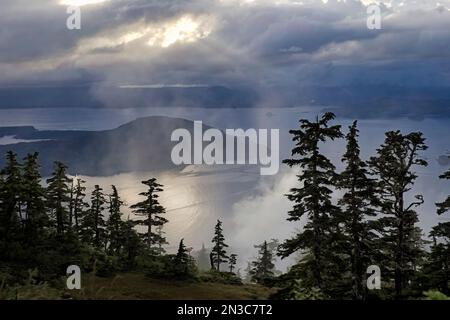 Sonnenstrahlen durchdringen die Wolken, die über dem Sitka Sound und Baranof Island hängen. Südost-Alaska erhält jährlich etwa 200 cm Regen, was ... ergibt Stockfoto