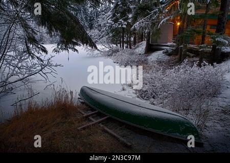 Frostiger Morgenschnee auf einem Kanu am Strand und Bäume rund um einen kleinen See in der Nähe des Mendenhall-Gletschers; Südost-Alaska, Alaska, Vereinigte Staaten von Amerika Stockfoto