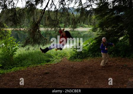 Zwei Freundinnen spielen auf einer Seilschaukel auf einer Insel im Tongass National Forest, wo sie mit ihren Familien im Südosten ... campen Stockfoto