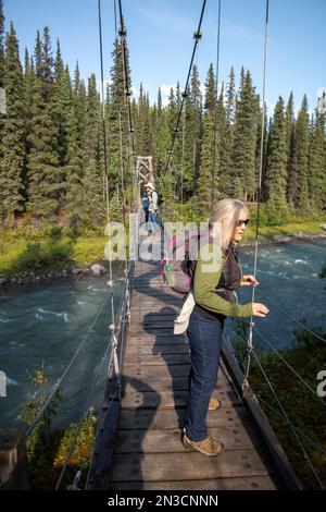 Wanderer über die Riley Creek Suspension Bridge auf dem Triple Lakes Trail Stockfoto