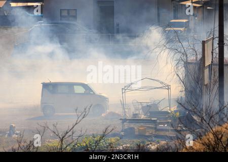 Dicker Rauch um ein kleines Auto auf einem Vorstadthof mit Gartenmöbeln Stockfoto