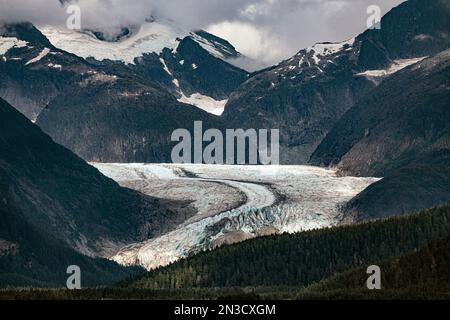 Massiver Gletscherfluss des Eagle Glacier, umgeben von schneebedeckten Bergen unter einem bewölkten Himmel in der Nähe von Juneau, Alaska, USA Stockfoto