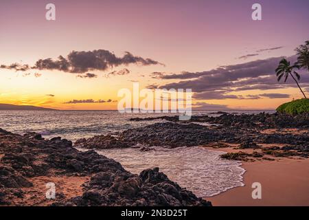 Warmes Sonnenlicht über einem Strand mit Palmen und Lavafelsen am goldenen Sand von Makena Cove auf Maui, Hawaii, USA Stockfoto