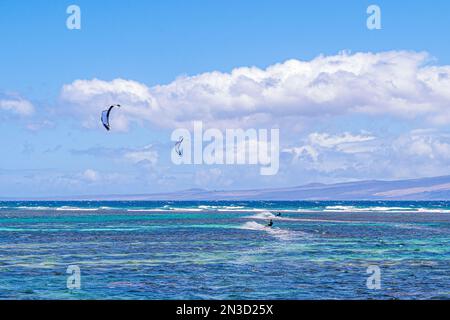 Zwei Kitesurfer reiten auf den Wellen vor der Küste von Shipwreck Beach in Lanai mit der Insel Maui in der Ferne; Hawaii, Vereinigte Staaten von Amerika Stockfoto