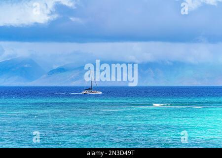 Ein motorisiertes Segelboot fährt durch das türkisfarbene Wasser der Pazifikküste vor Lahaina; Maui, Hawaii, USA Stockfoto