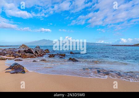 Surfen im Meer am Kapalua Beach mit bergigen hawaiianischen Inseln in der Ferne in West Maui; Maui, Hawaii, Vereinigte Staaten von Amerika Stockfoto