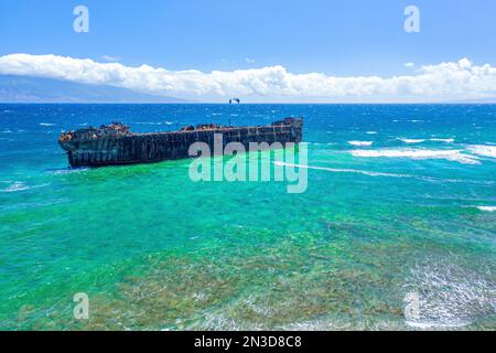 Ein Kiteboarder vor der Küste von Shipwreck Beach in Lanai, der auf dem Wasser in der Nähe eines alten Marineschiffs, das am Riff zerstört wurde, Kiteboarder fährt... Stockfoto