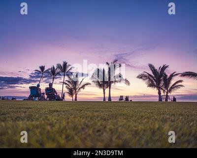 Blick von hinten auf Touristen, die in Rasenstühlen sitzen und den Sonnenuntergang über der Pazifikküste von Makena; Maui, Hawaii, Vereinigte Staaten von Amerika beobachten Stockfoto