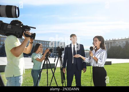 Professioneller Journalist und Bediener mit Videokameras, die im Freien Interviews führen Stockfoto