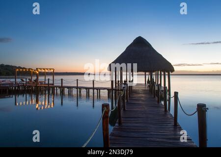 Silhouette der Tiki-Hütten-Gartenlaube am Dock im Rancho Encantado Eco-Resort & Spa in Bacalar bei Sonnenaufgang; Quintana Roo, Mexiko Stockfoto