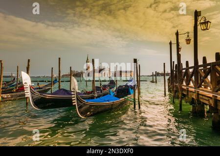 Blaue Gondeln entlang der Küste und Blick auf den Markusplatz über die Lagune in Venedig; Venedig, Venetien, Italien Stockfoto