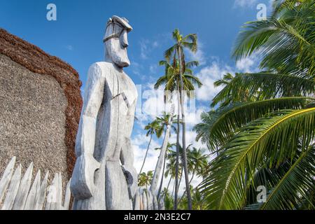 Holzstatue (Ki'i) einer hawaiianischen Gottheit vor einem Strohdach im Nationalpark Pu'uhonua o Hōnaunau, einer der am besten erhaltenen Ananci... Stockfoto