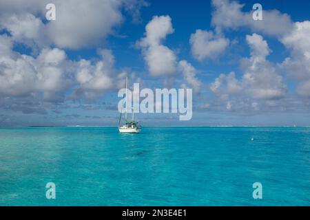 Ein einsames Segelboot vor der Küste im türkisfarbenen Wasser des Südpazifiks mit geschwollenen, weißen Wolken am blauen Himmel in der Lagune von Tahaa Stockfoto