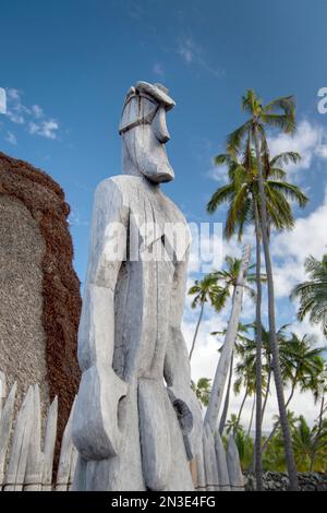 Holzstatue (Ki'i) einer hawaiianischen Gottheit vor einem Strohdach im Nationalpark Pu'uhonua o Hōnaunau, einer der am besten erhaltenen Ananci... Stockfoto