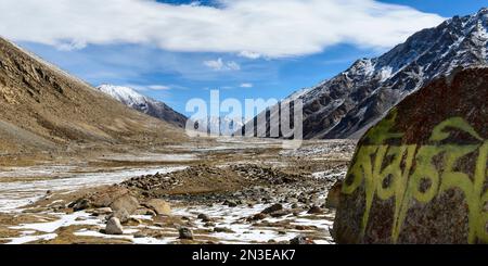 Eiskaltes Tal mit Mantra auf Felsen und schneebedeckten Bergen in den Ausläufern des Himalaya in der Region Ladakh Stockfoto