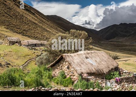 Bauerngemeinde im Lares-Tal mit den Anden über den Steinhäusern mit Strohdächern; Lares-Tal, Cusco, Peru Stockfoto