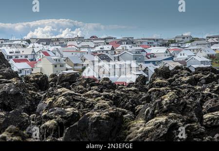 Lavaströme mit Blick auf die Häuser in der Stadt auf der Insel Heimaey, Teil der Westman Inseln, eine Inselgruppe mit etwa 15 Inseln im Süden der COAs... Stockfoto