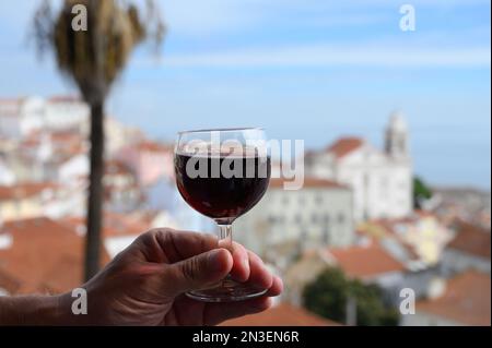 Hand mit einem Glas des portugiesischen Weins porto im Café im Freien am Aussichtspunkt in der farbenfrohen Altstadt von Lissabon, Portugal Stockfoto