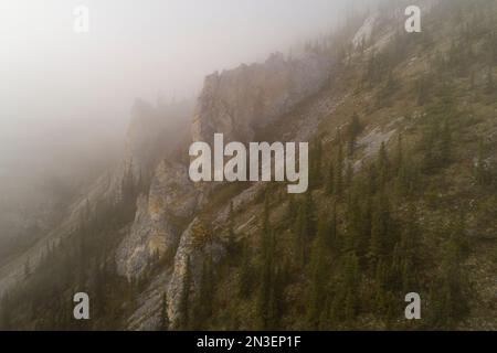 Luftbild eines nebeligen Berges in den Ogilvie Mountains mit Felsenbändern am Berghang. Die nebelige Atmosphäre führt zur Stimmungslosigkeit ... Stockfoto