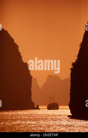 Karstformationen und traditionelles vietnamesisches Segelboot (thung Chai) bei Sonnenuntergang in der Bai Tu Long Bucht in der Halong Bucht, die zum UNESCO-Weltkulturerbe gehört Stockfoto