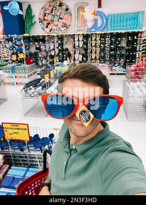 Ein Mann probiert eine riesige Sonnenbrille in einem Supermarkt Stockfoto