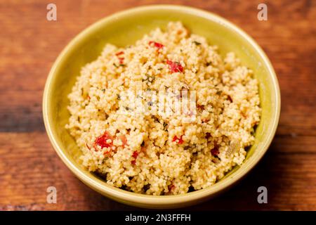 Tabbouleh-Salat mit Couscous, Gewürzen und Tomaten - auf einem gelben Teller auf Holzhintergrund. Traditioneller orientalischer Salat, Vorspeise. Stockfoto