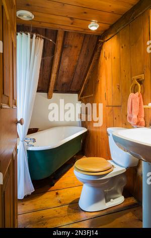 Badezimmer mit grüner, 1880er Fuß großer Badewanne, Toilette mit Holzsitz und Sockelwaschbecken im oberen Stockwerk im alten Canadiana Haus aus dem Jahre 1750. Stockfoto