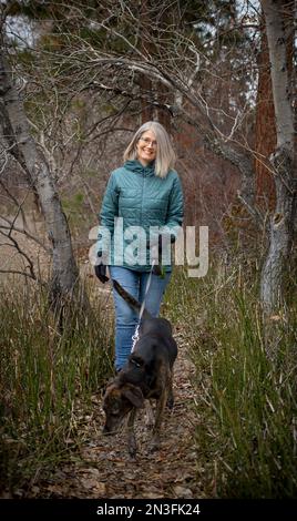 Eine Frau führt ihren Hund in einem bewaldeten Park, Fourth Street Park, Lake Country, BC, Kanada; British Columbia, Kanada Stockfoto