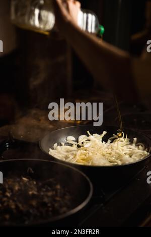 Zwiebeln werden in einer Pfanne gebraten und mit Olivenöl besprüht. Dunkler Hintergrund. Stockfoto